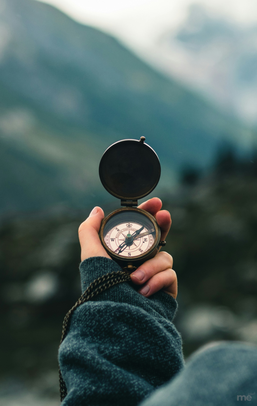 Close-up of a person’s hand holding an antique brass compass against a blurred mountain backdrop, symbolizing inner guidance and clarity of direction.