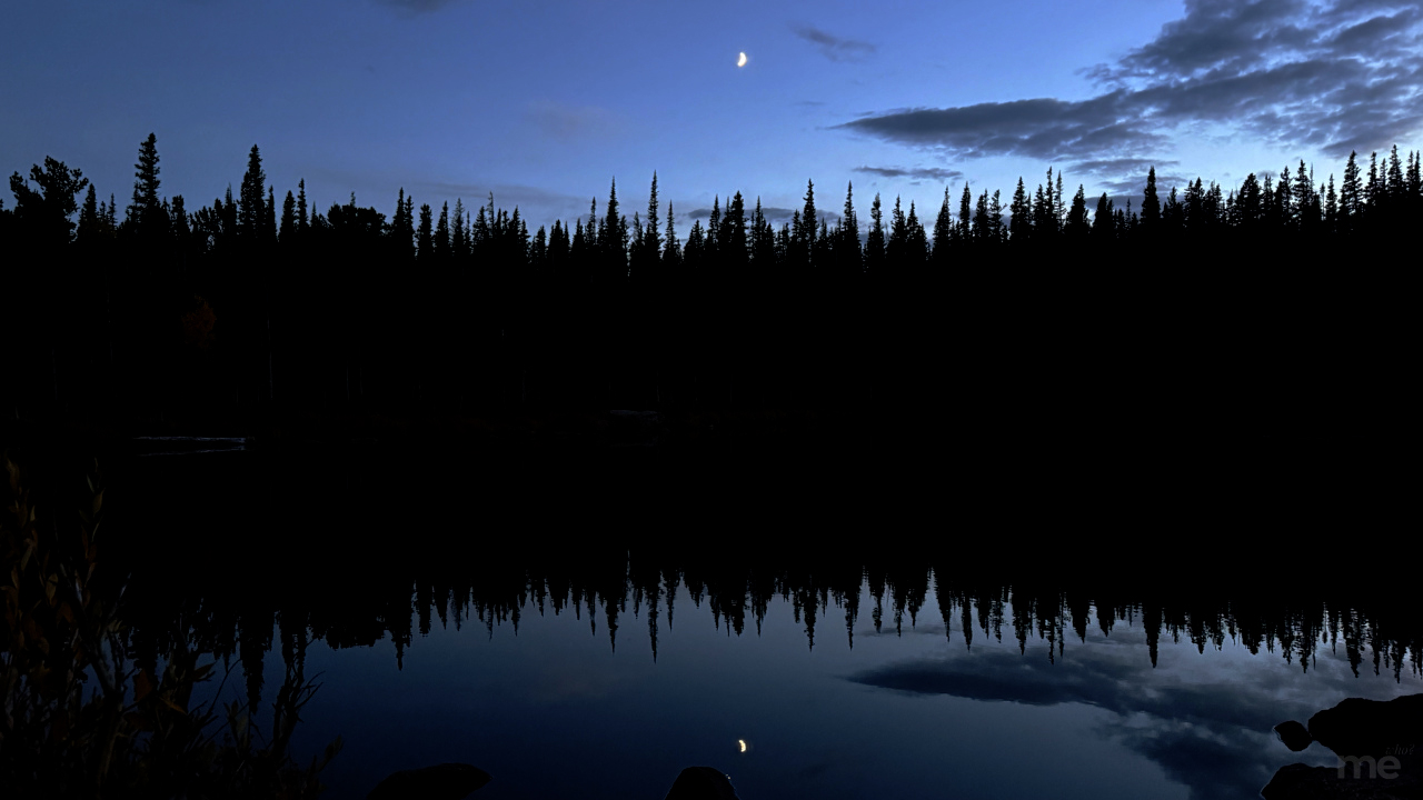 blaming-myself-featured-image a calm twilight lake reflecting a dark pine forest and a small crescent moon in still water.