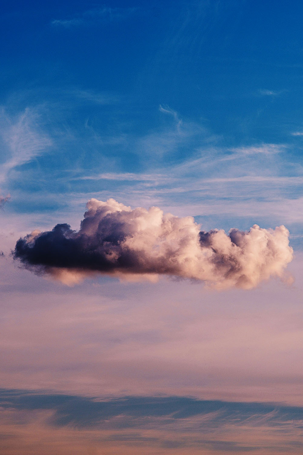 A single, fluffy cumulus cloud floating in a gradient sky that transitions from soft pink to a clear blue.